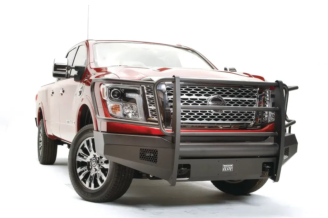 Fab Fours Black Steel Elite front bumper with full guard on a red Nissan TITAN XD, driver-side front three-quarter view, showing the full grille guard, headlight hoops and mesh light openings