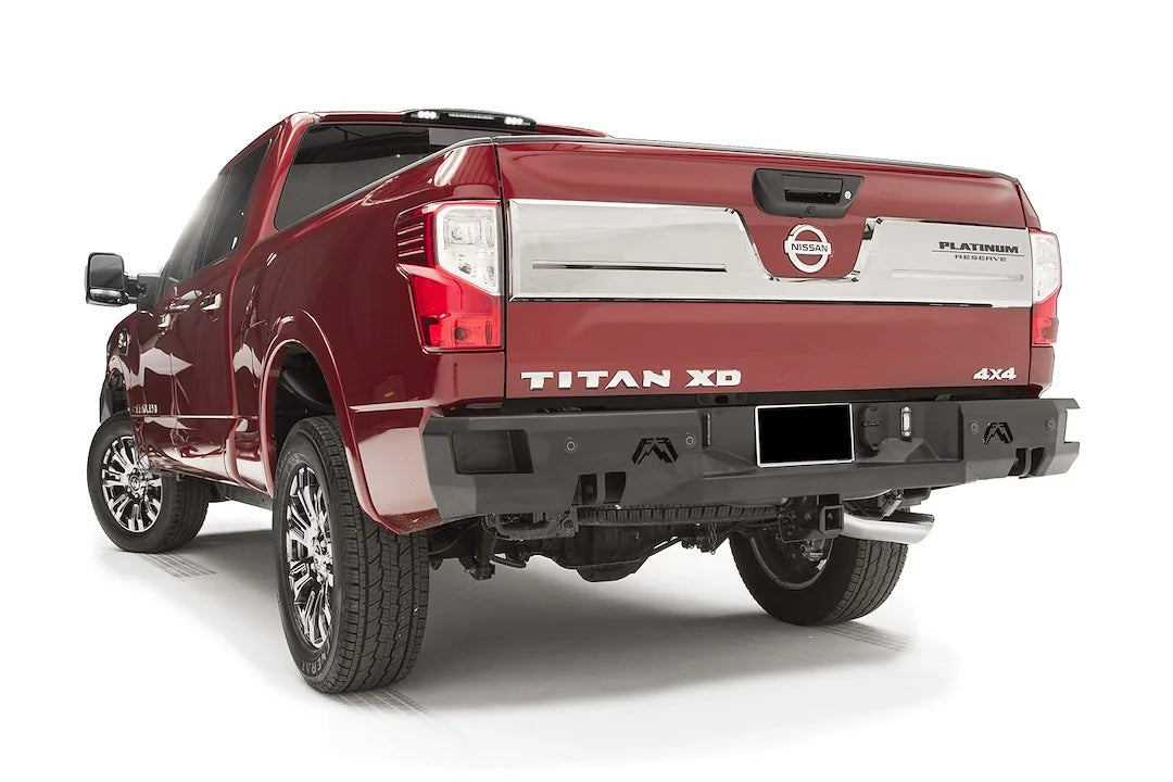 Fab Fours Premium rear bumper on a red Nissan Titan XD, driver-side rear three-quarter view, with parking sensors, Fab Fours logo cutouts, and hitch receiver