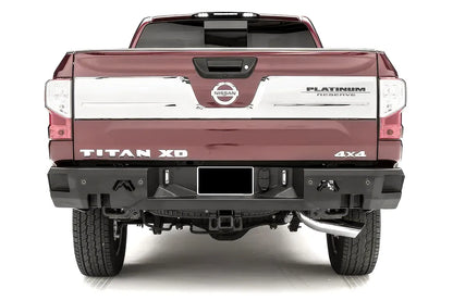 Fab Fours Premium rear bumper on a red Nissan Titan XD, straight rear view, with parking sensors, center license plate area, Fab Fours logo cutouts, and hitch receiver