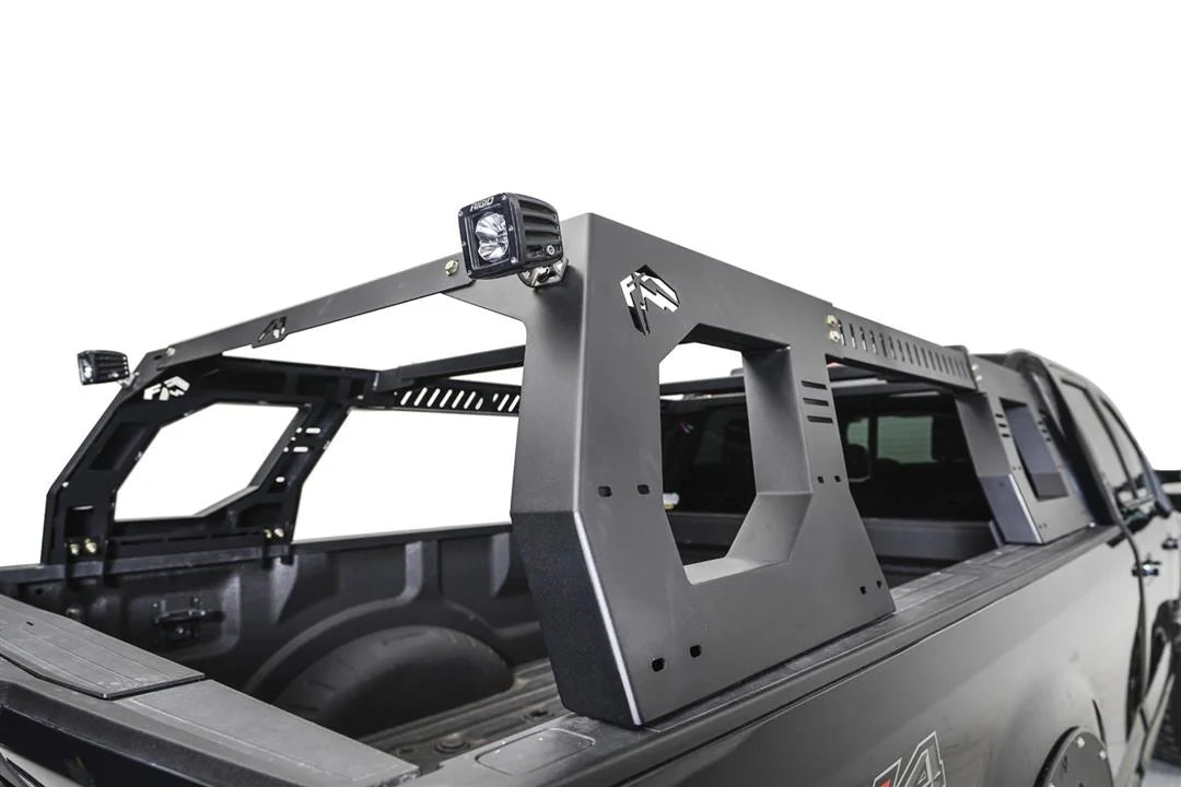 ab Fours Adjustable Overland Rack in a black full-size pickup bed, rear passenger-side view, showing the matte black side panels with Fab Fours logo cutouts, vented crossbars and RIGID cube lights