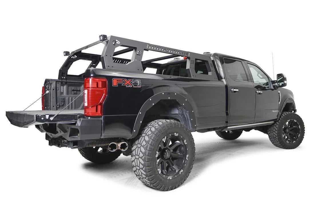 Fab Fours Adjustable Overland Rack on a black full-size pickup truck, rear passenger-side view with the tailgate down, showing the side panels, crossbars and corner-mounted cube lights