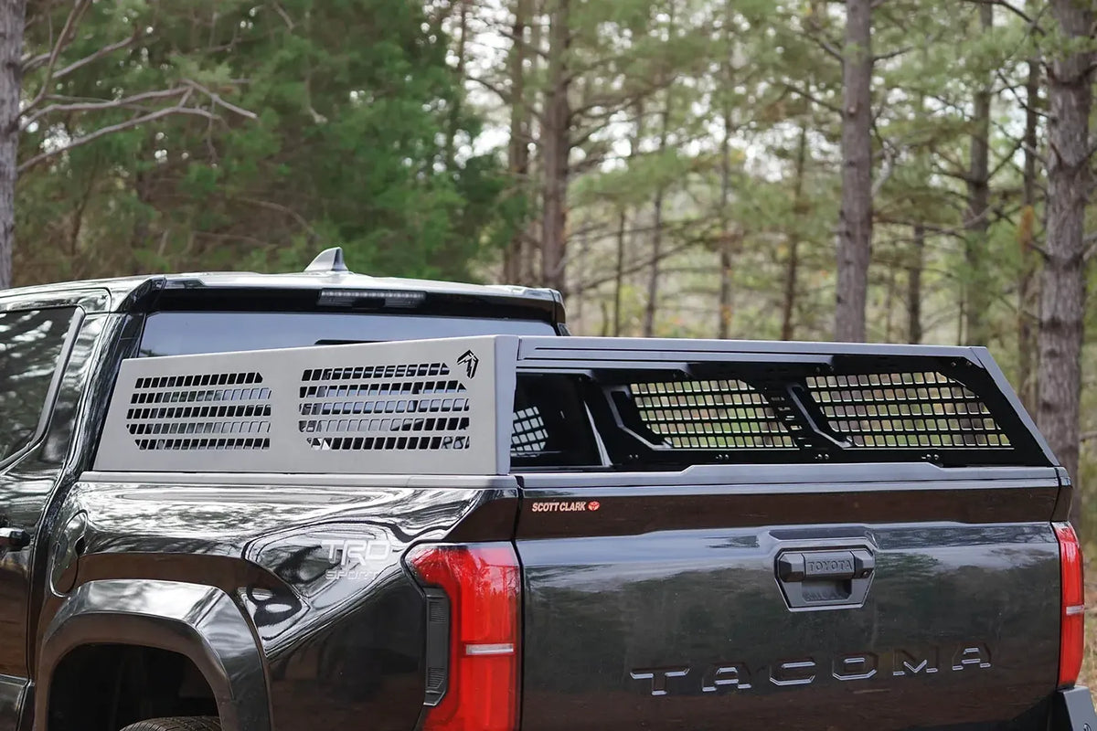 Fab Fours half rack with perforated side panels and mesh bed panels on a black Toyota Tacoma in the woods, driver-side rear view