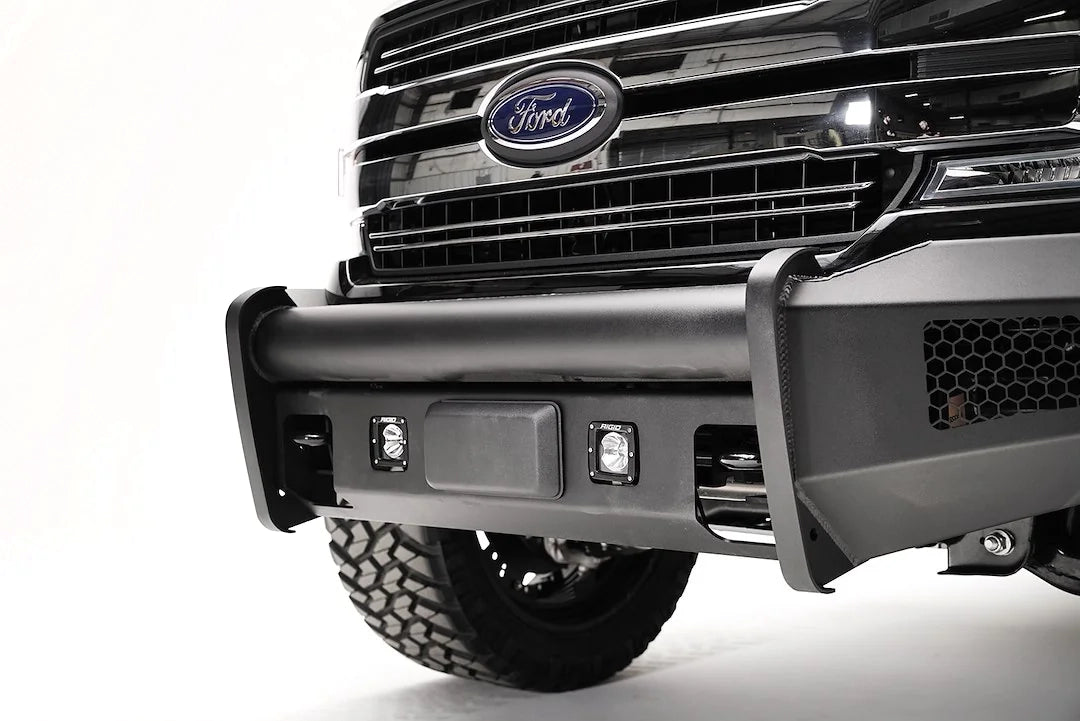Fab Fours Elite adaptive cruise control relocation bracket on a black Ford F-150, close-up of the bumper center, showing the relocated sensor plate between cube lights