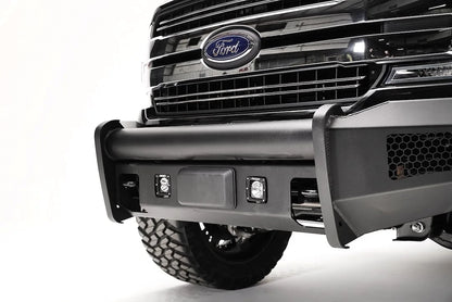 Fab Fours Elite adaptive cruise control relocation bracket on a black Ford F-150, close-up of the bumper center, showing the relocated sensor plate between cube lights