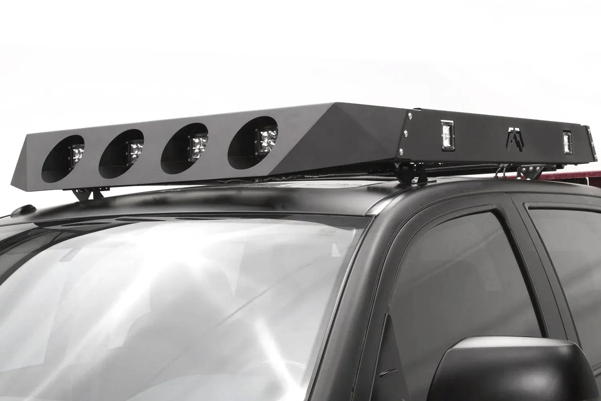 Fab Fours roof rack on a black pickup truck cab, with four round light openings holding cube lights across the front, side-mounted LED lights, and Fab Fours logo, angled front view
