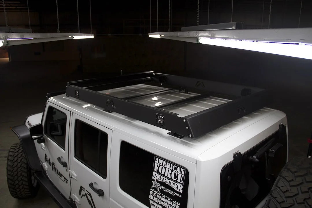 Fab Fours roof rack on a white Jeep Wrangler JK, driver-side view in a dim garage, showing the rack mounted on the hardtop with crossbars and cube lights