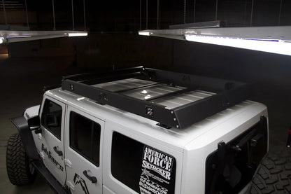 Fab Fours roof rack on a white Jeep Wrangler JK, driver-side view in a dim garage, showing the rack mounted on the hardtop with crossbars and cube lights