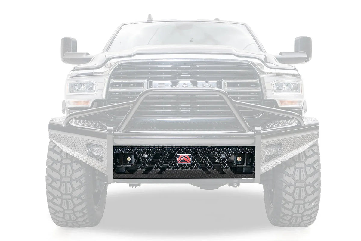 Fab Fours replacement lower guard on a Ram HD front bumper, front view, with the black diamond tread plate guard highlighted against the faded-out truck, showing angled cutouts, sensor holes, D-ring mounts and a red Fab Fours badge