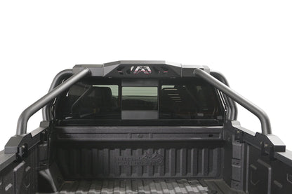Fab Fours Sport Rack installed in a pickup truck bed, rear view, showing the matte black tubular hoops and center light pod housing with Fab Fours logo cutout behind the cab