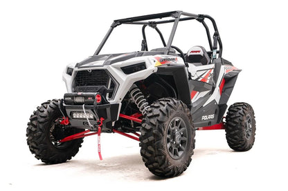 Fab Fours SxS winch bumper on a white Polaris RZR XP, driver-side front three-quarter view, with Warn Axon winch, LED light bar, and red D-ring shackles
