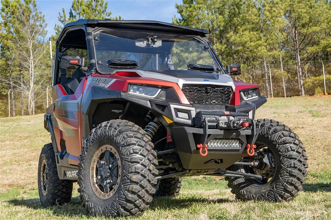 Fab Fours SxS winch bumper on a red Polaris General 1000 parked on grass, passenger-side front three-quarter view, with Warn Axon winch, LED light bar, and orange D-ring shackles