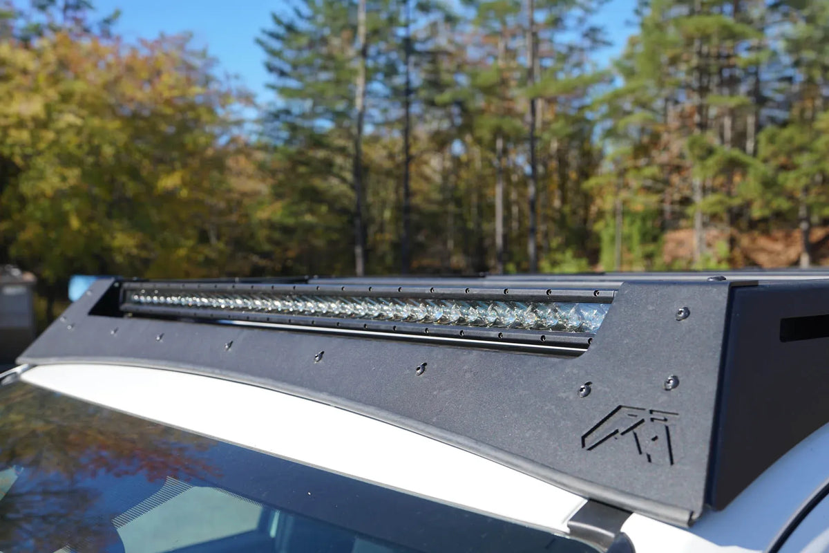 Close-up of the Fab Fours Roof Rack front fairing on a Toyota 4Runner, showing the integrated LED light bar, Fab Fours logo cutout and textured black finish