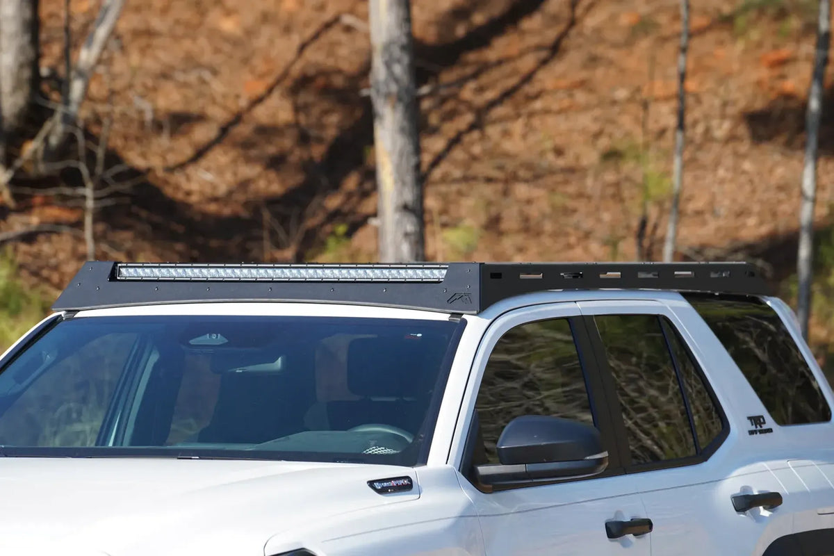 Fab Fours Roof Rack on a white Toyota 4Runner TRD Off-Road outdoors, driver-side profile, showing the low-profile rack with an LED light bar set into the front fairing