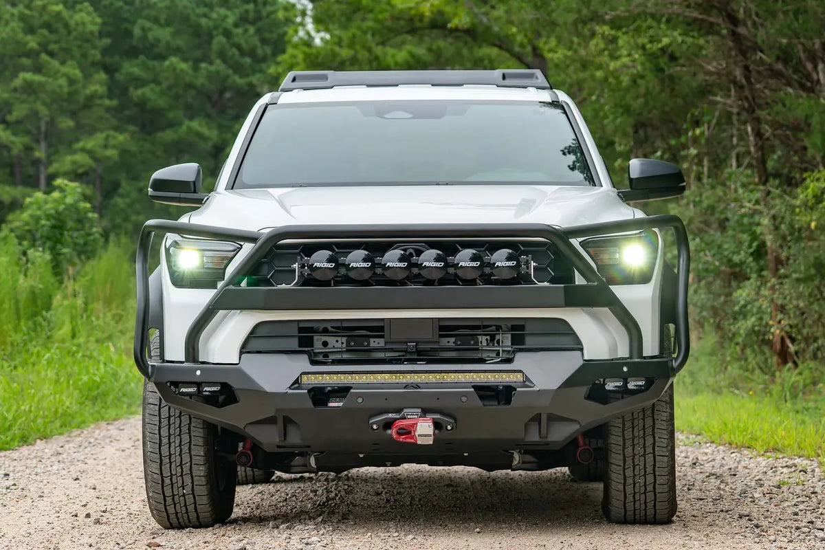 Fab Fours Matrix front winch bumper with full guard on a white Toyota 4Runner on a gravel road, straight-on front view, showing the full guard, LED light bar and winch with red hook