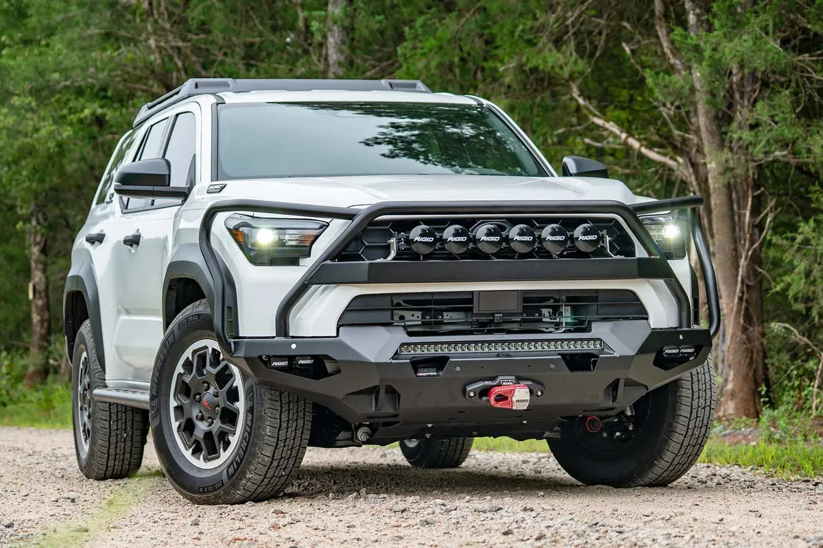 Fab Fours Matrix front winch bumper with full guard on a white Toyota 4Runner outdoors, passenger-side front three-quarter view, showing the full guard, light bar and winch