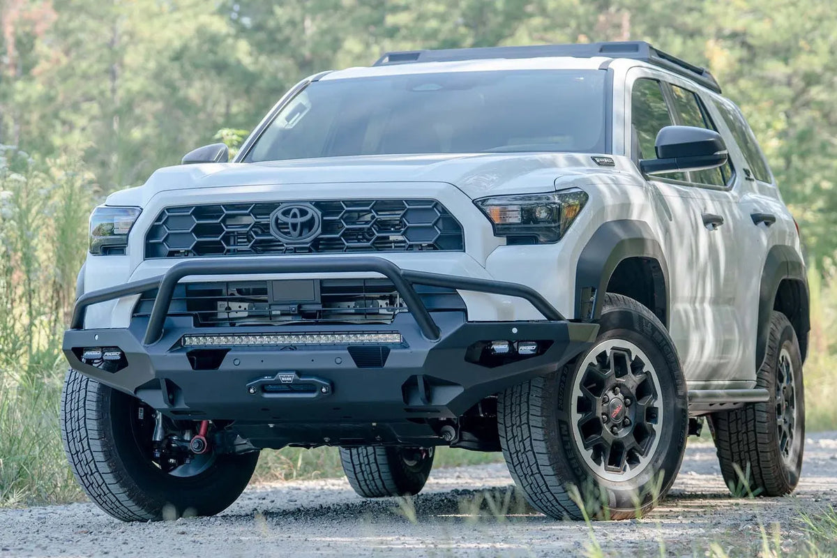 Fab Fours Matrix front winch bumper with pre-runner guard on a white Toyota 4Runner on a gravel road, driver-side front three-quarter view, showing the tube hoop, LED light bar and winch fairlead