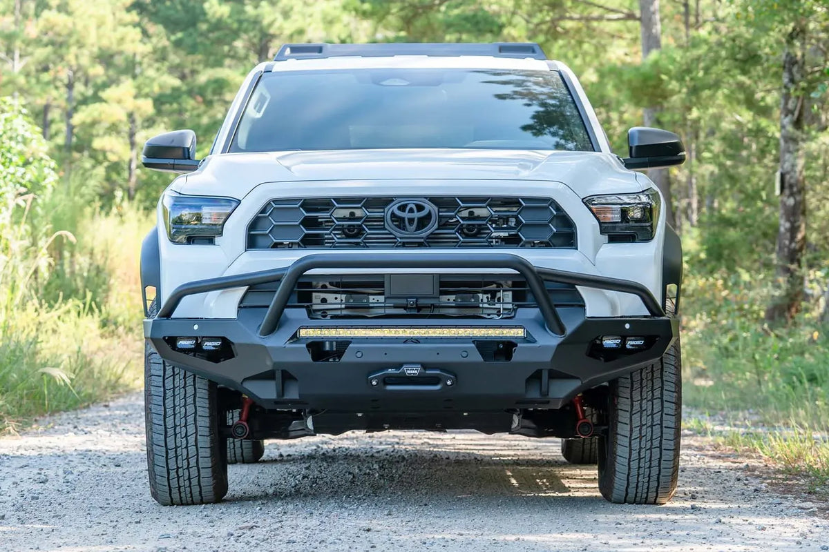 Fab Fours Matrix front winch bumper with pre-runner guard on a white Toyota 4Runner on a gravel road, straight-on front view, showing the tube hoop, LED light bar and winch fairlead