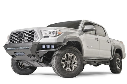 Fab Fours Hybrid front bumper on a silver Toyota Tacoma, front three-quarter view from the driver side, showing pod lights, LED light bar and winch opening
