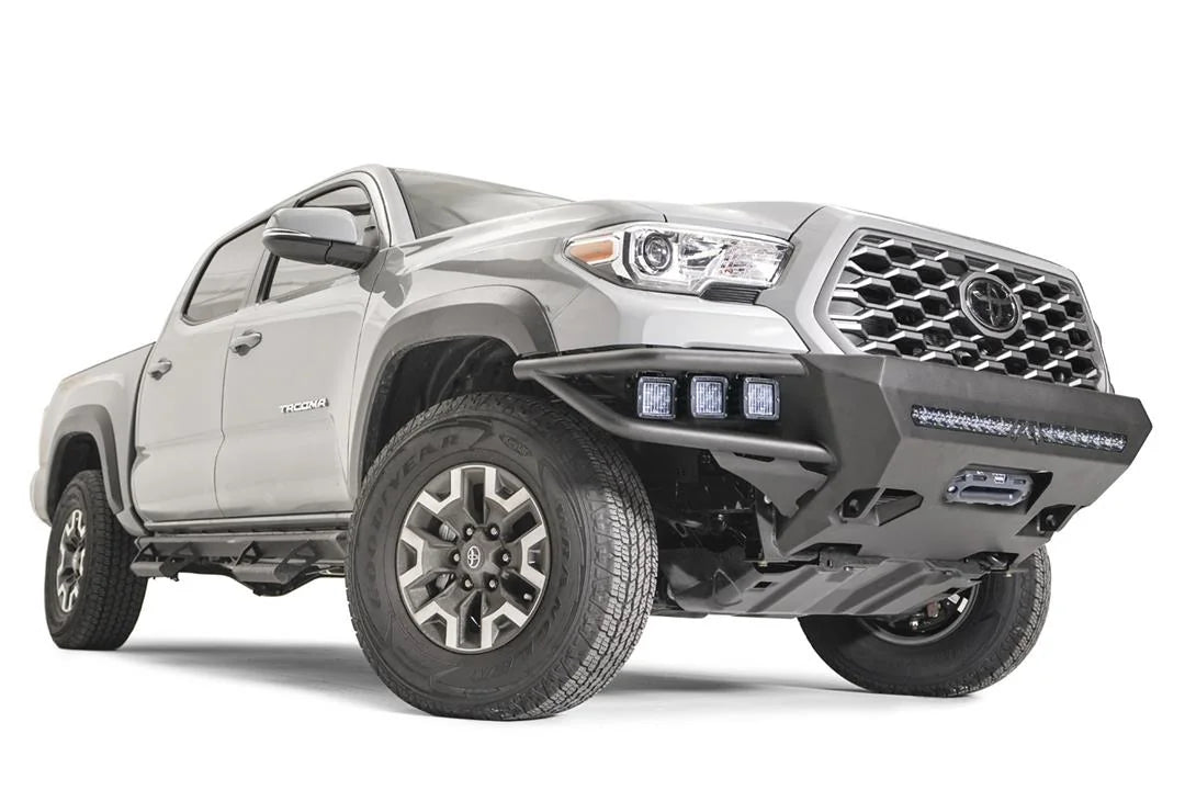 Fab Fours Hybrid front bumper on a silver Toyota Tacoma, front three-quarter view from the passenger side, showing integrated pod lights, LED light bar and skid plate