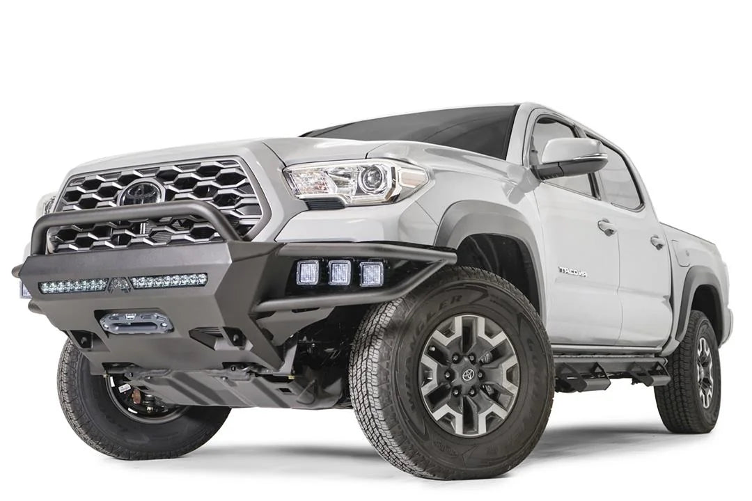 Fab Fours Hybrid front bumper with pre-runner guard on a silver Toyota Tacoma, front three-quarter view from the driver side, showing the pre-runner hoop, pod lights, LED light bar and winch opening