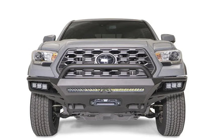 Fab Fours Hybrid front bumper with pre-runner guard on a silver Toyota Tacoma, front view, showing the pre-runner hoop, the LED light bar, cube lights and centre winch opening