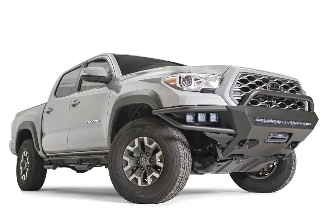 Fab Fours Hybrid front bumper with pre-runner guard on a silver Toyota Tacoma, front three-quarter view from the passenger side, showing the pre-runner hoop, integrated pod lights, LED light bar and skid plate