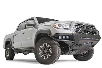 Fab Fours Hybrid front bumper with pre-runner guard on a silver Toyota Tacoma, front three-quarter view from the passenger side, showing the pre-runner hoop, integrated pod lights, LED light bar and skid plate