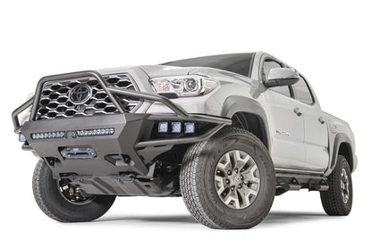 Fab Fours Hybrid front bumper with full guard on a silver Toyota Tacoma, front three-quarter view from the driver side, showing the full grille guard, pod lights, LED light bar and winch opening