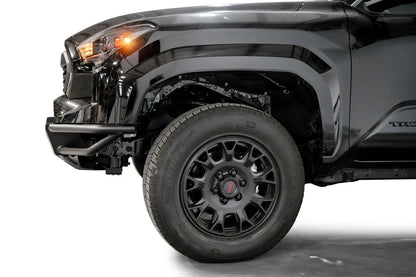 Fab Fours Hybrid front bumper on a black Toyota Tacoma, close-up of the front corner from the side, showing the tube wing, bumper end and wheel clearance