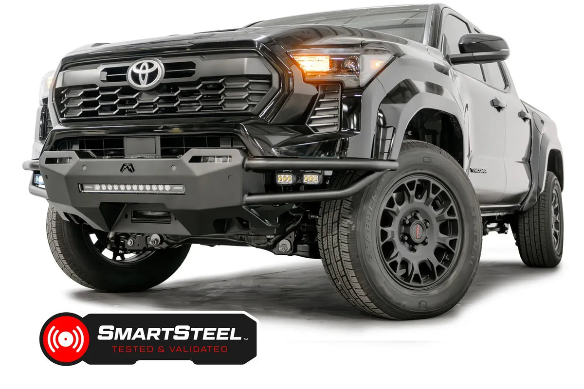 Fab Fours Hybrid front bumper on a black Toyota Tacoma, front three-quarter view from the passenger side, showing the tube wings, LED light bar and cube lights