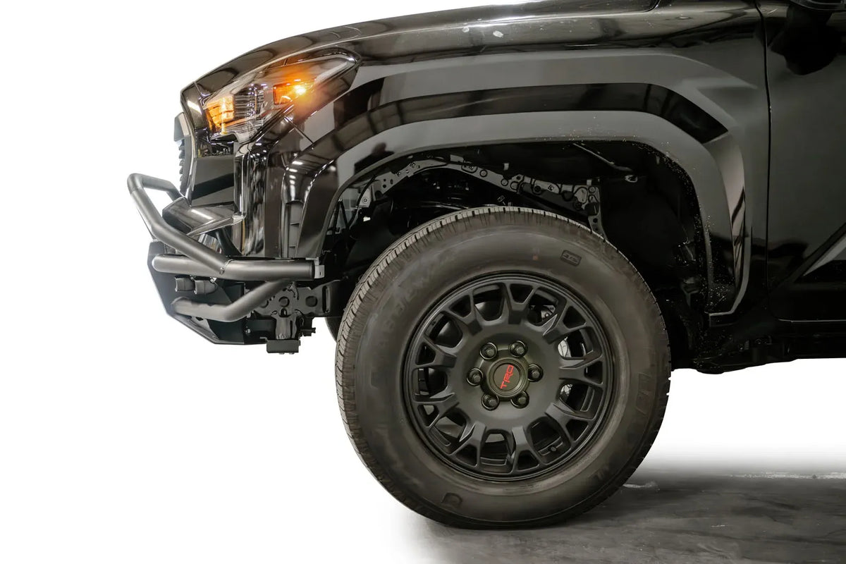 Fab Fours Hybrid front bumper with pre-runner guard on a black Toyota Tacoma, close-up of the front corner from the side, showing the pre-runner tube, bumper end and wheel clearance