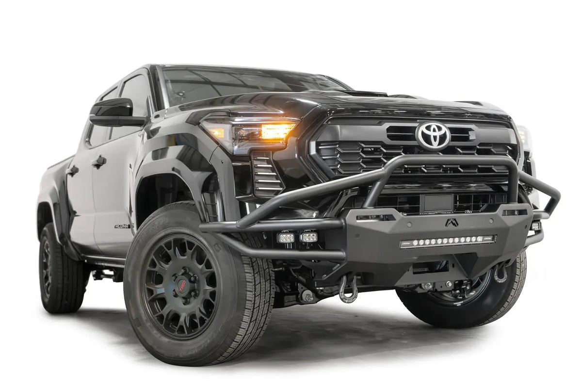 Fab Fours Hybrid front bumper with pre-runner guard on a black Toyota Tacoma, front three-quarter view from the passenger side, showing the pre-runner hoop, tube wings and LED light bar