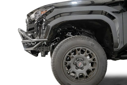 Fab Fours Ultra Light front bumper with pre-runner guard on a black Toyota Tacoma, close-up of the front corner from the side, showing the pre-runner tube, bumper end and wheel clearance