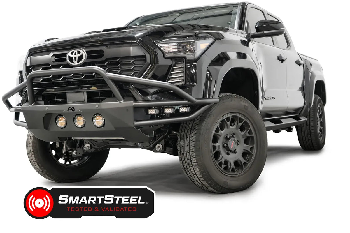 Fab Fours Ultra Light front bumper with pre-runner guard on a black Toyota Tacoma, front three-quarter view from the passenger side, showing the pre-runner hoop, three round lights and tube wings