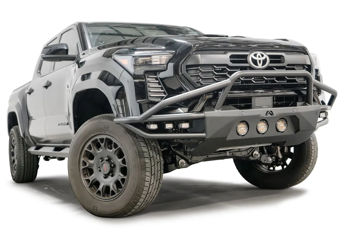 Fab Fours Ultra Light front bumper with pre-runner guard on a black Toyota Tacoma, front three-quarter view from the passenger side, showing the pre-runner hoop, tube wings and round lights