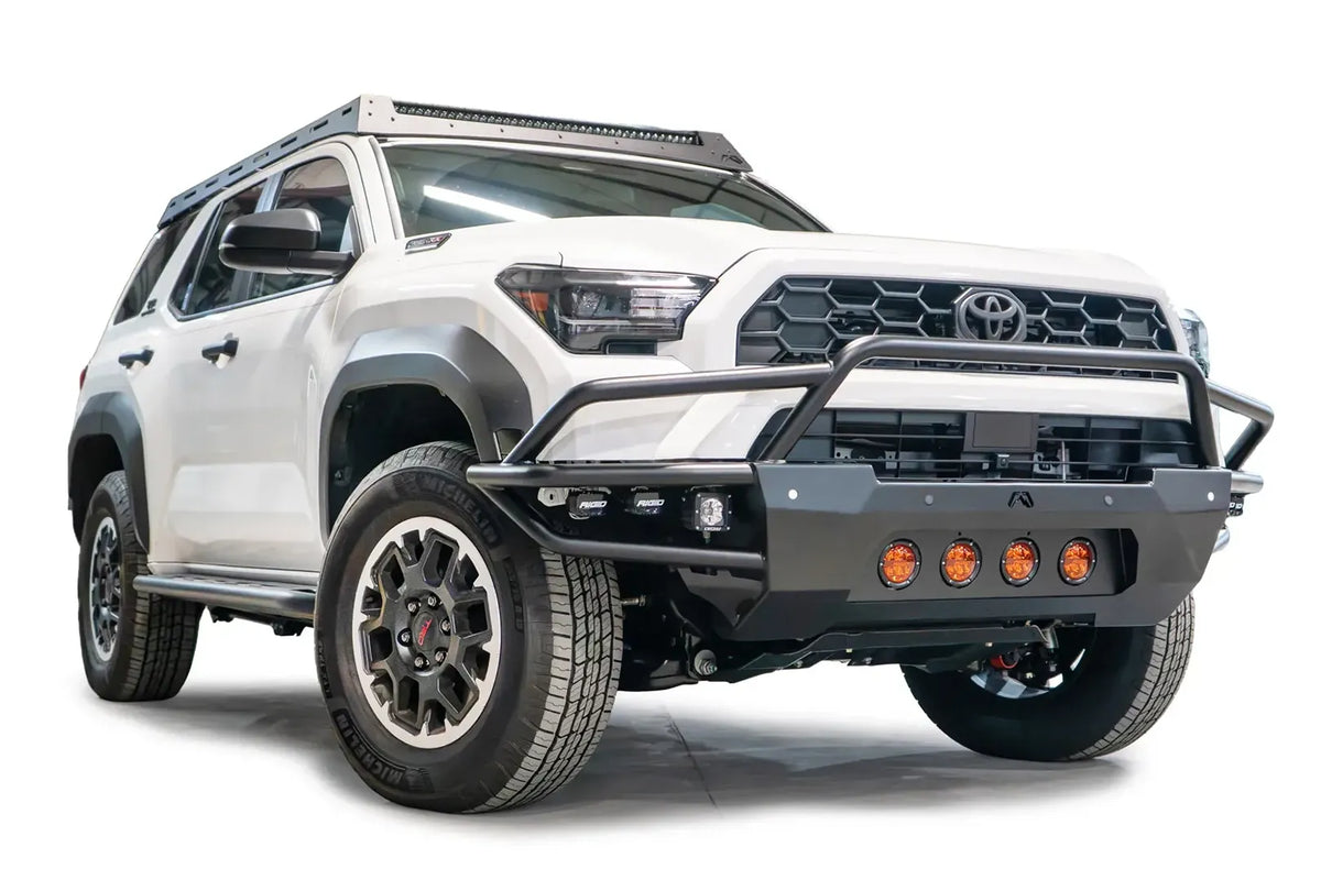 Fab Fours Ultra Light Front Bumper with guard on a white 2025 Toyota 4Runner, front passenger-side view, with the tubular guard over the grille, amber round lights and side-mounted RIGID cube lights