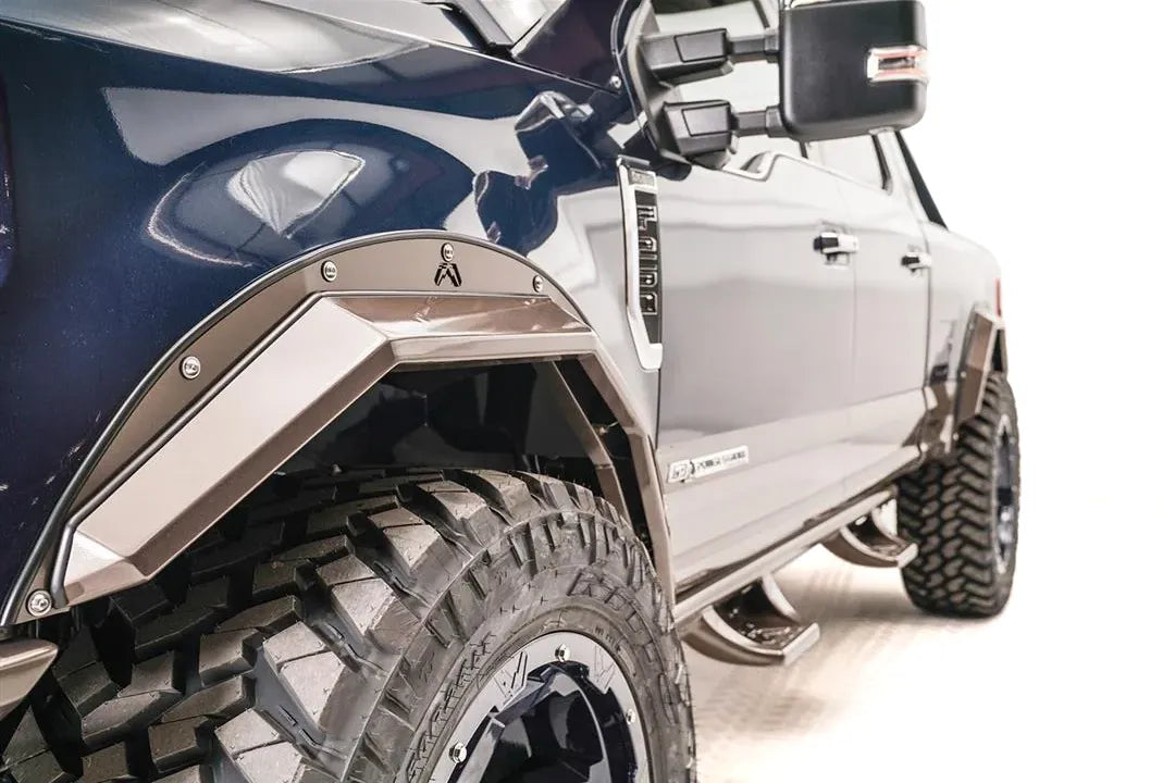 Close-up of Fab Fours bronze open fender flare with Fab Fours logo on the driver-side front wheel of a blue Ford F-250 Super Duty