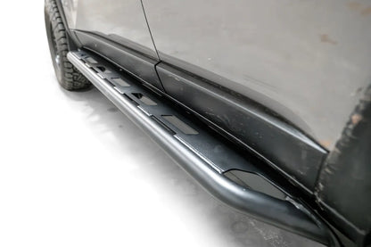 Fab Fours Rock Step slider on a silver Toyota Land Cruiser, angled view along the rocker, showing the matte black tube rail and step plate with slotted cutouts
