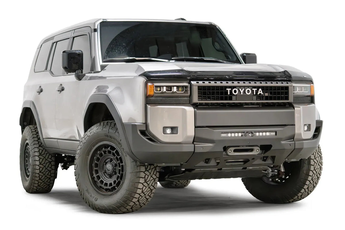 Fab Fours Hidden Winch Mount on a silver Toyota Land Cruiser, front three-quarter view from the passenger side, showing the low-profile winch plate, LED light bar and fairlead