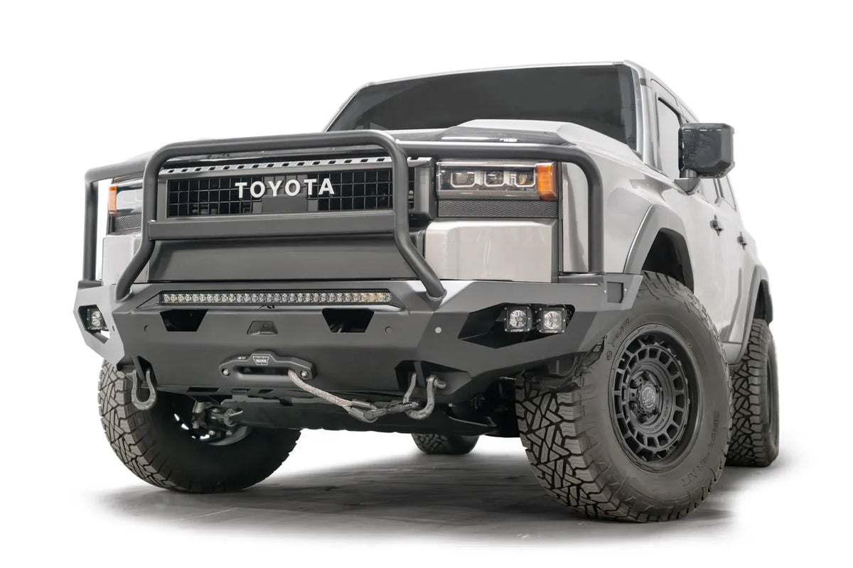 Fab Fours Matrix front bumper with full guard on a silver Toyota Land Cruiser, front three-quarter view from the driver side, showing the full grille guard, LED light bar and winch line