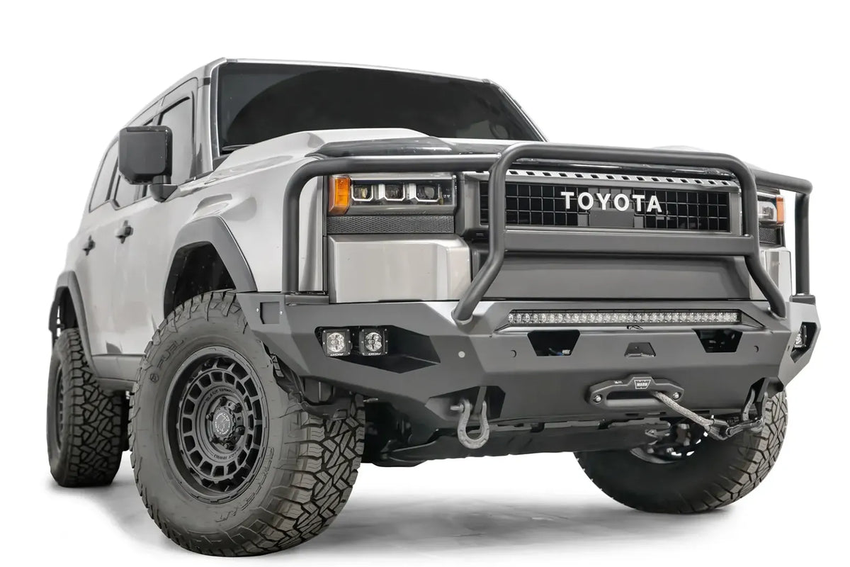 Fab Fours Matrix front bumper with full guard on a silver Toyota Land Cruiser, front three-quarter view from the passenger side, showing the full grille guard, LED light bar, cube lights and winch fairlead