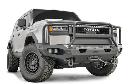 Fab Fours Matrix front bumper with full guard on a silver Toyota Land Cruiser, front three-quarter view from the passenger side, showing the full grille guard, LED light bar, cube lights and winch fairlead