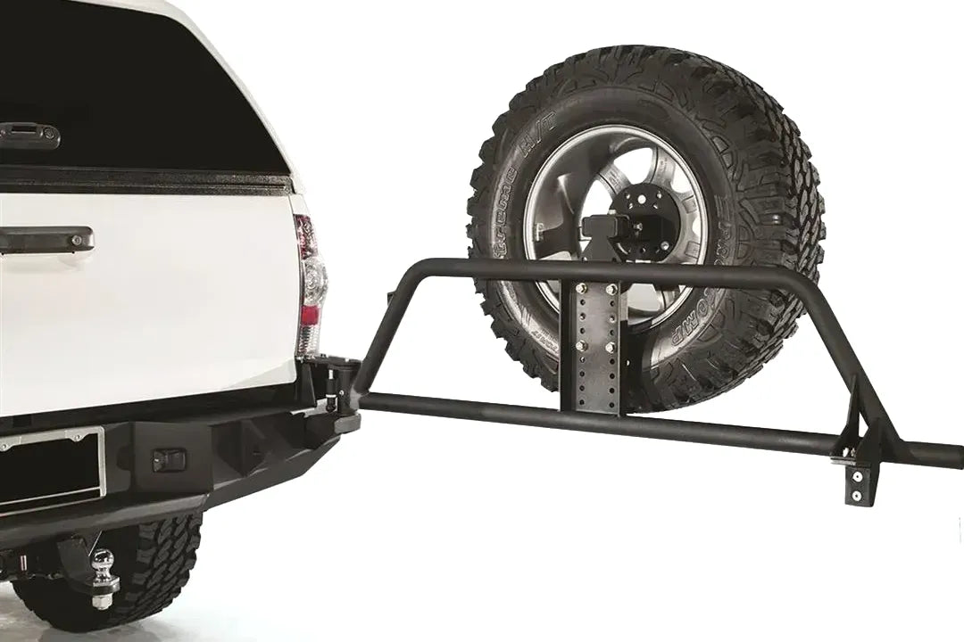 Fab Fours swing-out spare tire carrier on a white Toyota Tacoma, swung open from the rear bumper to show the tubular arm, adjustable tire mount and latch