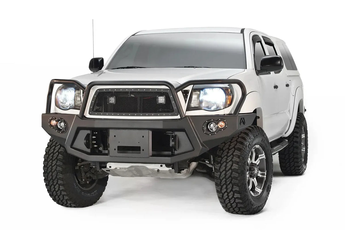 Fab Fours Premium front bumper with full guard on a white Toyota Tacoma, front view, showing the full grille guard, recessed winch plate and round fog lights