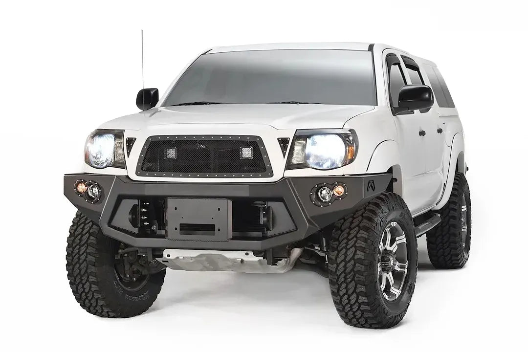 Fab Fours Premium front bumper on a white Toyota Tacoma, front view, showing the recessed winch plate, round fog lights and angled end caps