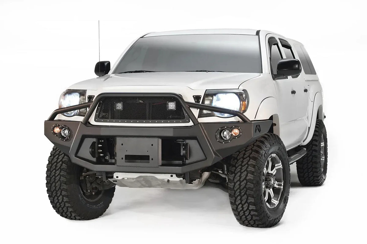 Fab Fours Premium front bumper with pre-runner guard on a white Toyota Tacoma, front view, showing the pre-runner hoop, recessed winch plate and round fog lights