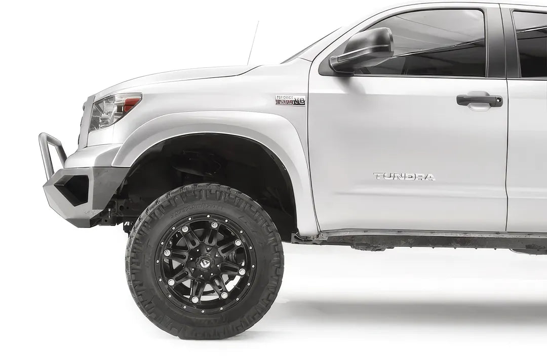 Fab Fours Vengeance front bumper with pre-runner guard on a silver Toyota Tundra, close-up of the front corner from the side, showing the pre-runner hoop, the bumper end and wheel clearance