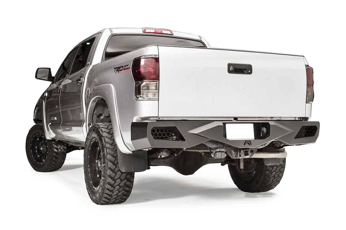 Fab Fours Vengeance rear bumper on a silver Toyota Tundra, rear three-quarter view from the driver side, showing the honeycomb light cutouts, centre plate recess and receiver hitch