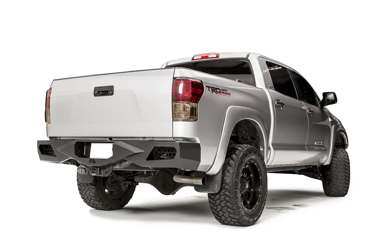 Fab Fours Vengeance rear bumper on a silver Toyota Tundra, rear three-quarter view from the passenger side, showing the honeycomb light cutouts, plate recess and angled end caps