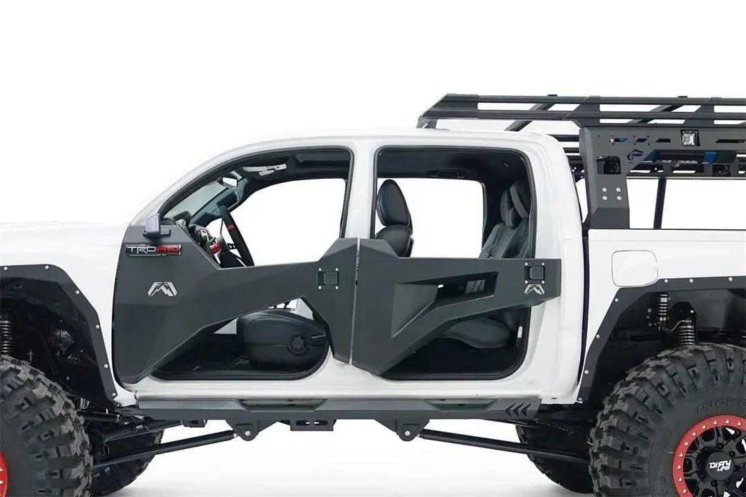 Fab Fours trail doors on a white Toyota Tacoma, driver-side close-up, showing the open-top faceted steel front and rear doors with the Fab Fours logo and paddle latches